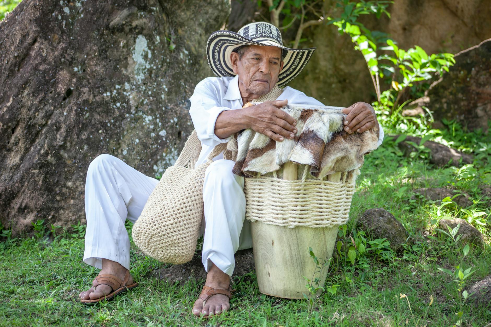 elderly colombian man sitting on grass holding traditional drum